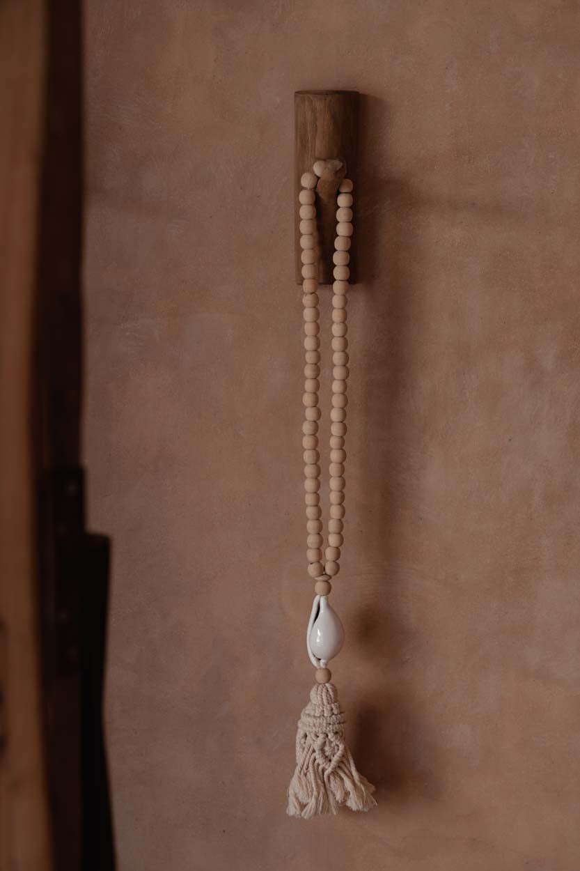 The Ocean Whisper Necklace — detail of macramé tassel and cowrie shell, warm light
