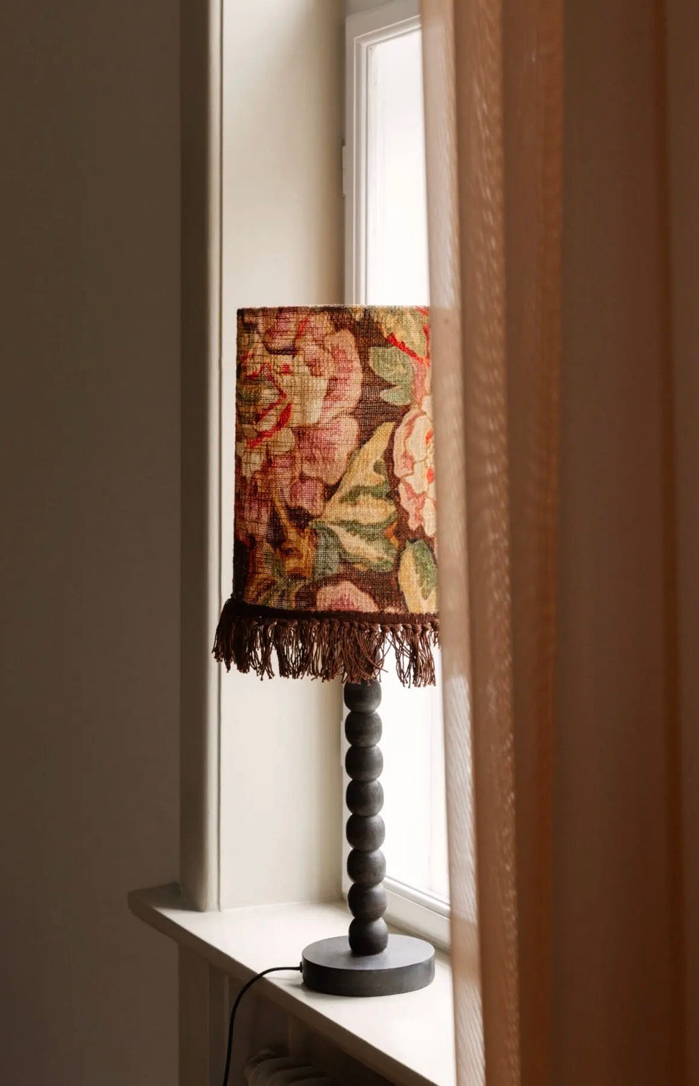Suzette Lamp Shade styled on bobbin-turned dark wood lamp base on windowsill with natural light