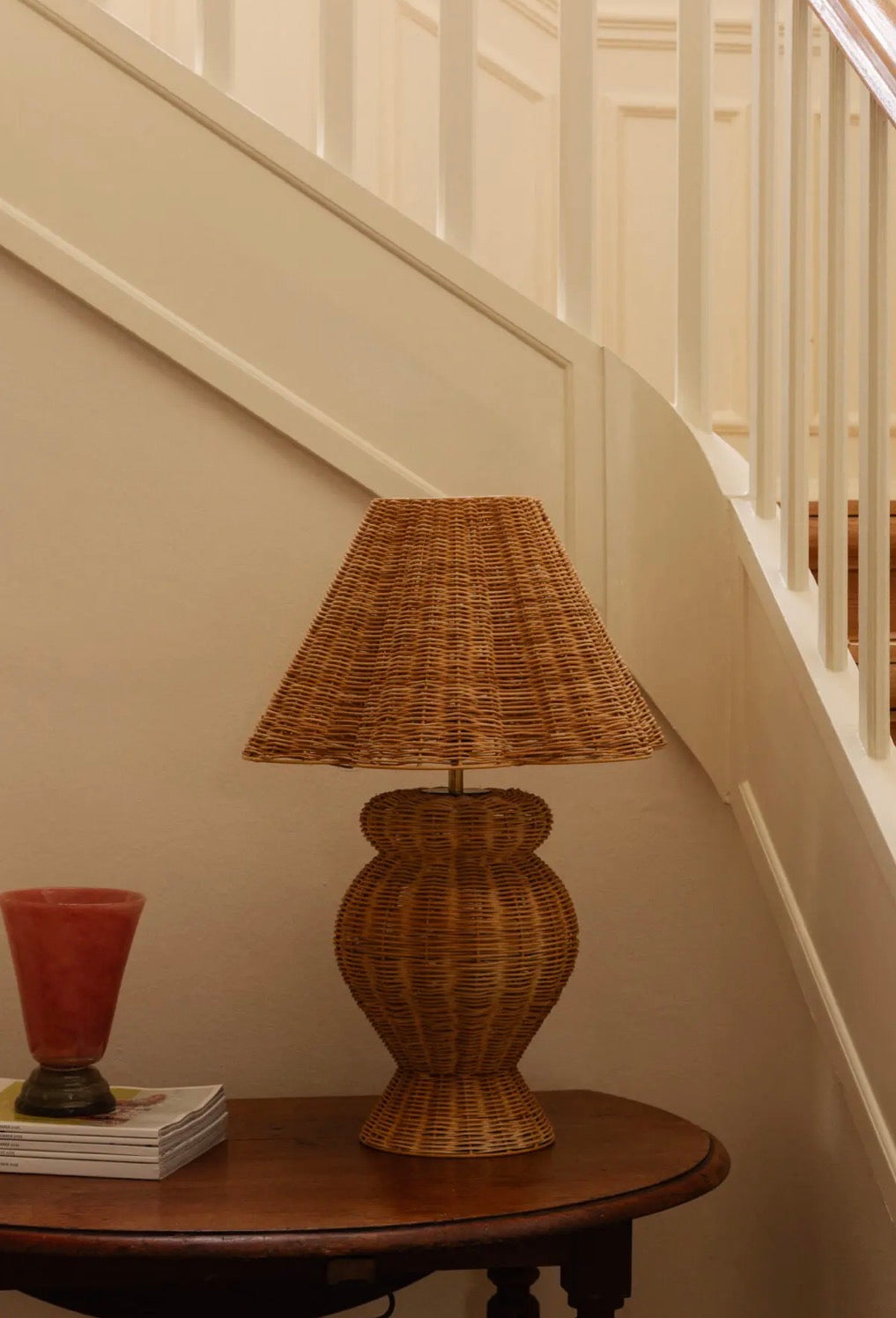 Bani Table Lamp styled on antique round side table beneath white staircase with warm ambient light