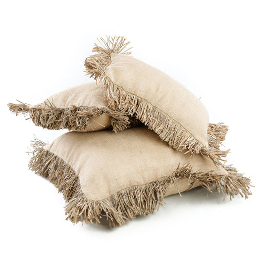 The Jute Bonita Cushion Cover in natural, styled on a white linen sofa with raffia fringe detail