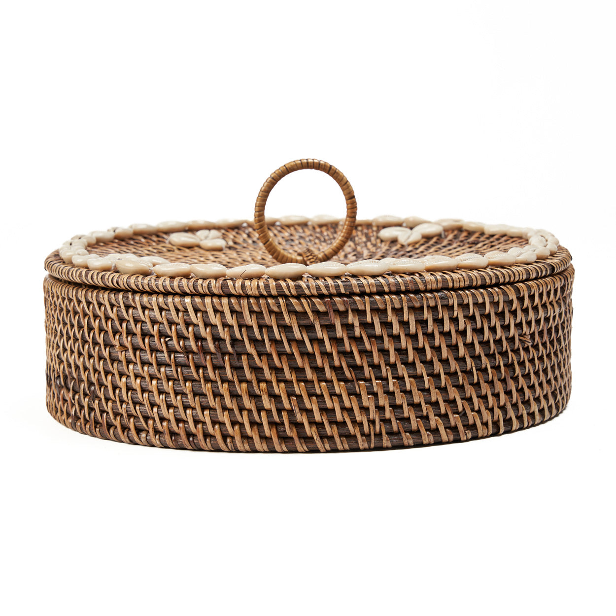 The Rattan Compartment Basket in natural brown rattan with cowrie shell lid, styled on a terracotta surface beside a large ceramic vase