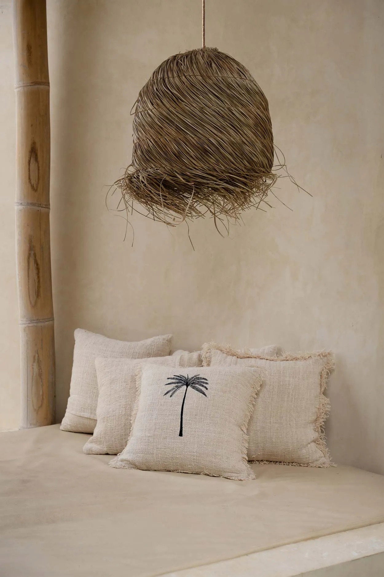 The Gili Palm Cushion Cover — lifestyle shot on bench with rattan pendant lamp