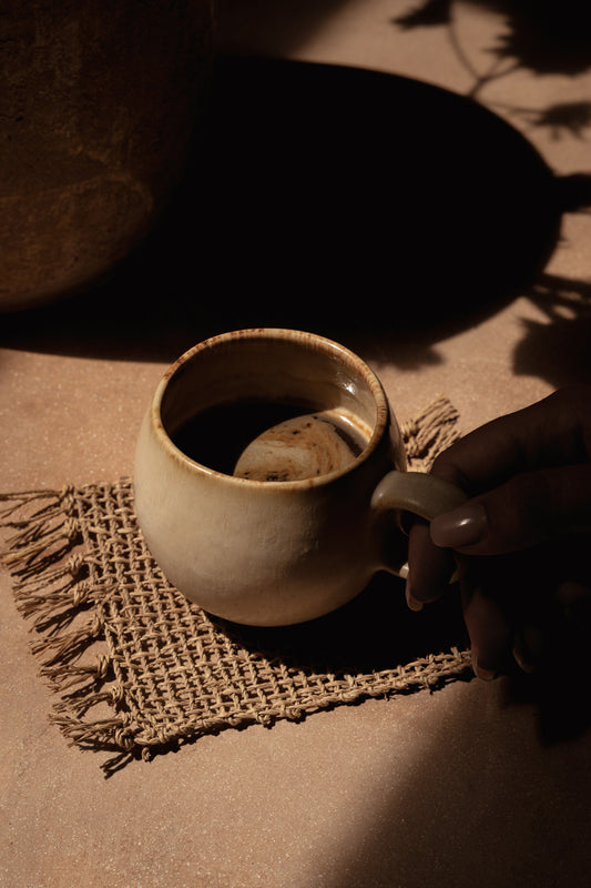 The Isey Seagrass Coaster — Natural, lifestyle with ceramic mug on warm surface
