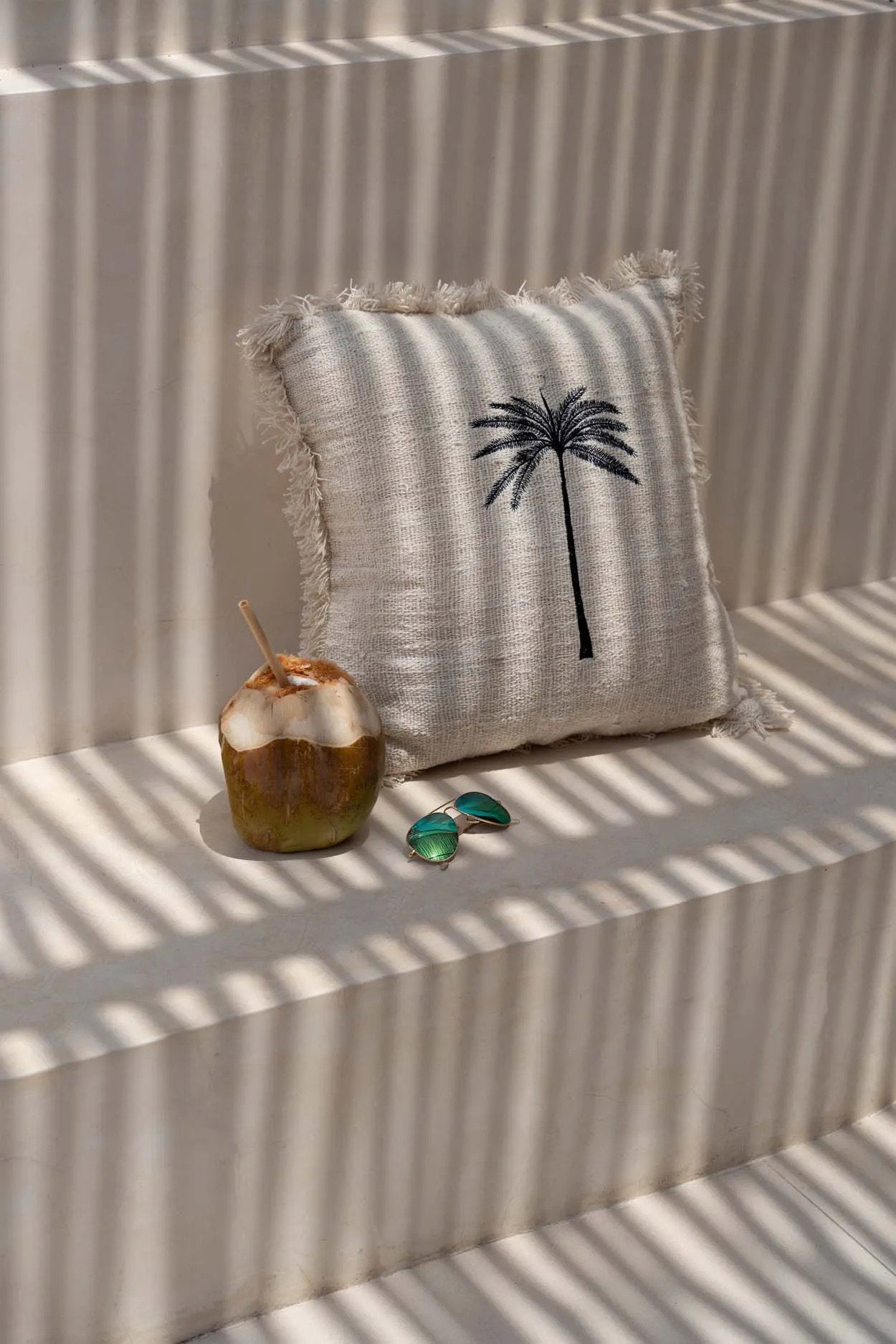 The Gili Palm Cushion Cover — lifestyle shot on curved stone bench with dried grasses