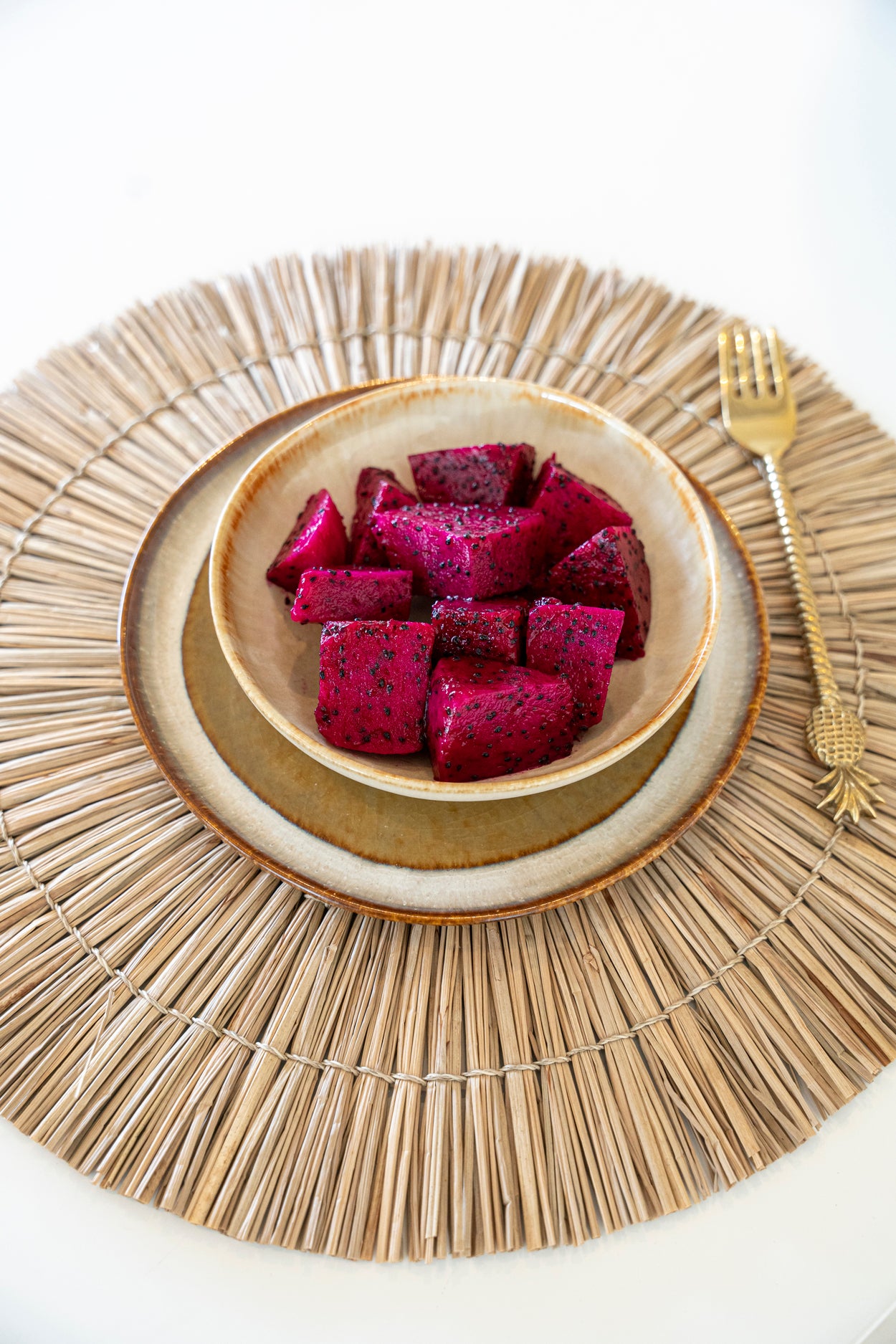 The Comporta Appetizer Plate styled on a woven rattan placemat with dragon fruit and a golden fork