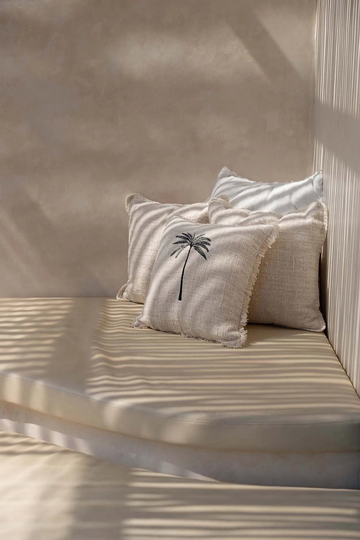 The Gili Palm Cushion Cover — lifestyle shot on striped daybed with coconut and sunglasses