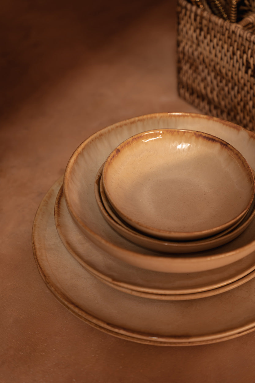 The Cascais Dinner Plate styled on a warm terracotta surface beside stacked bowls and a rattan basket