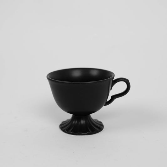 Yin Cup Black — matte black porcelain cup with wide bowl form on sculpted scalloped foot, side view on grey background