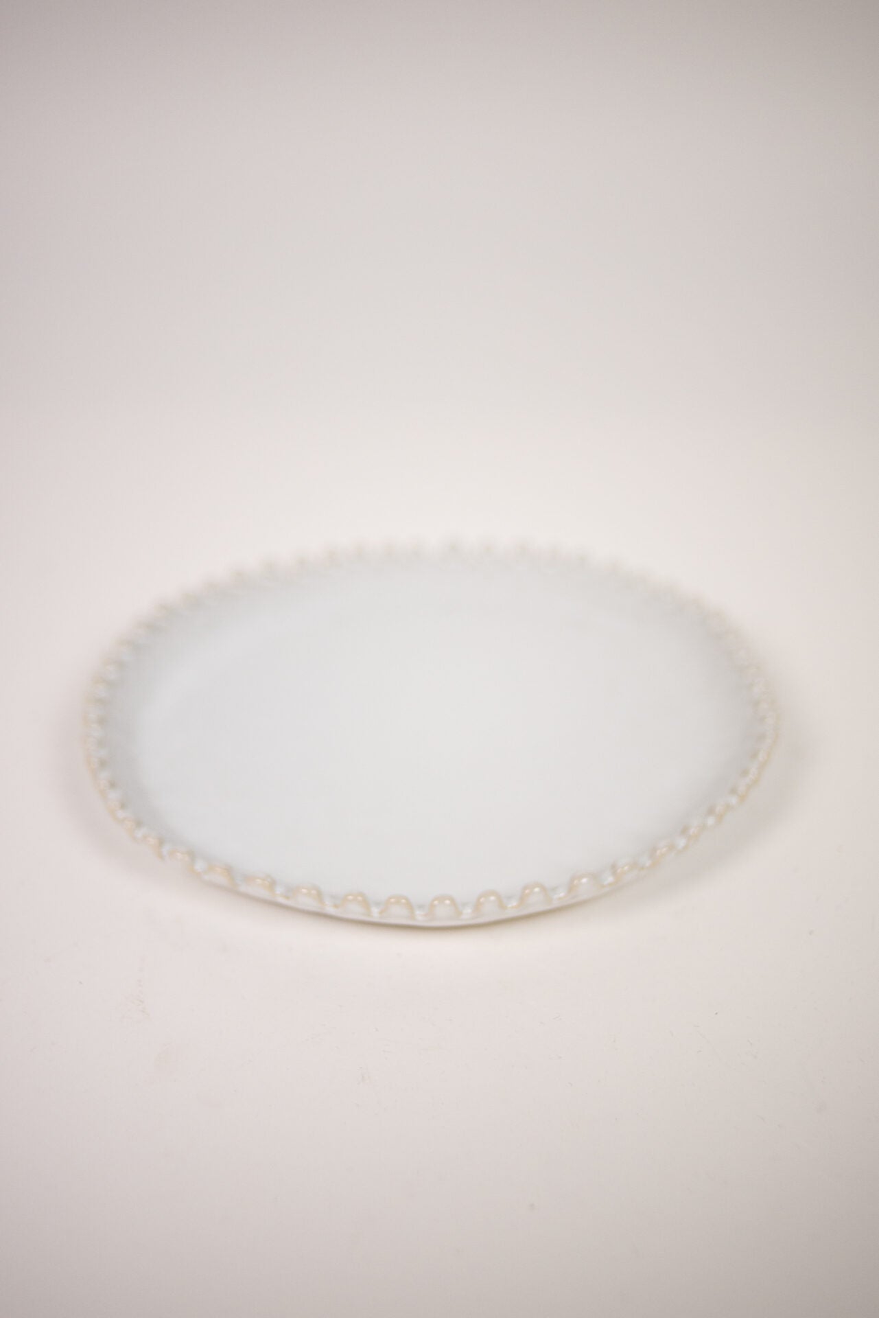 Eden Dinner Plate White — round white stoneware plate with textured scalloped rim, top view on warm white background