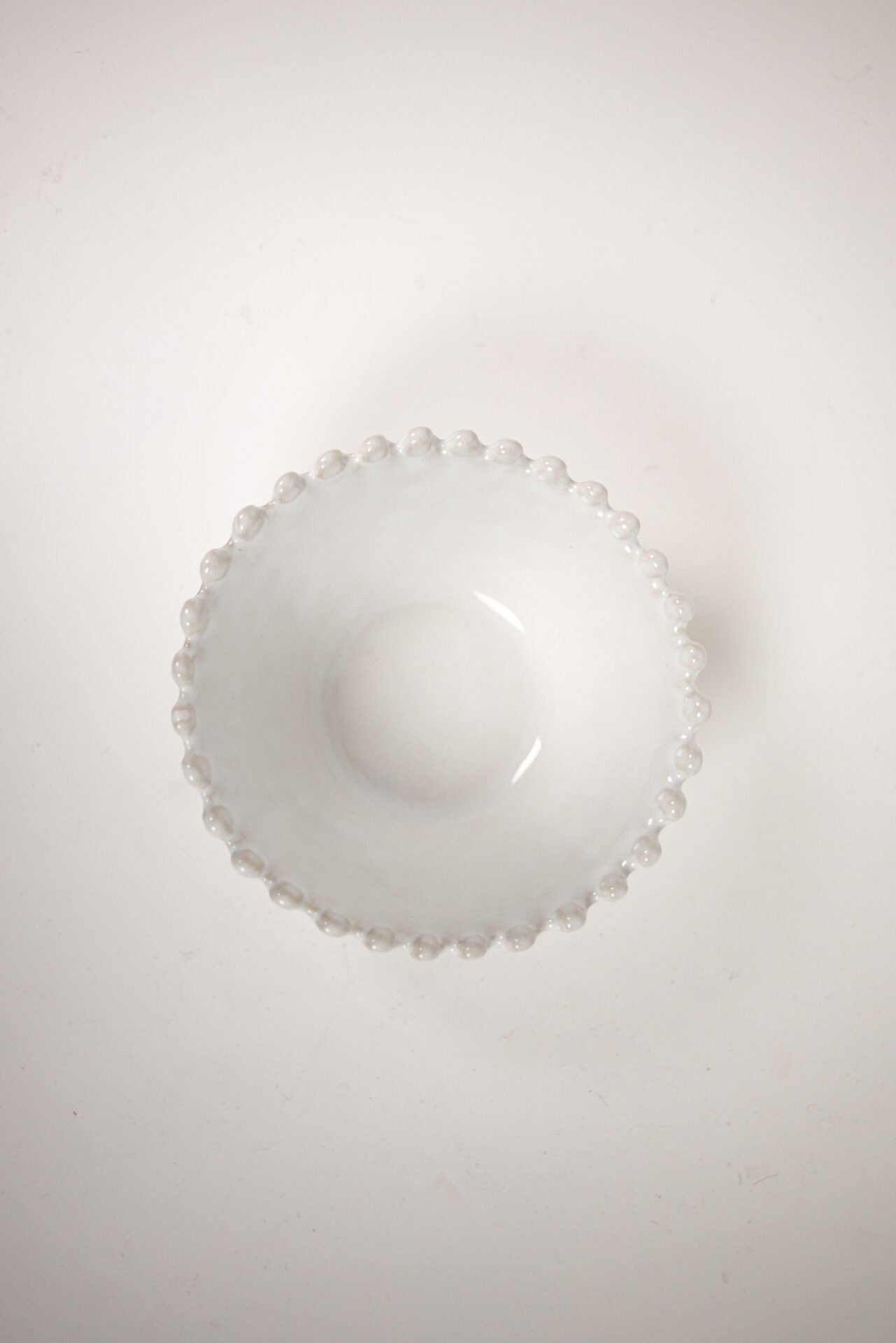 Eden Bowl White — wide shallow white stoneware bowl with beaded rim, top view on warm white background