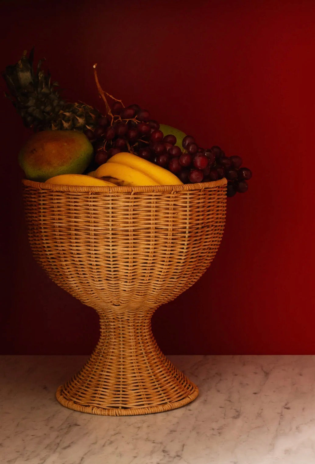 Beth Decoration Bowl filled with tropical fruit — bananas, grapes, avocado — on marble surface against dark red wall