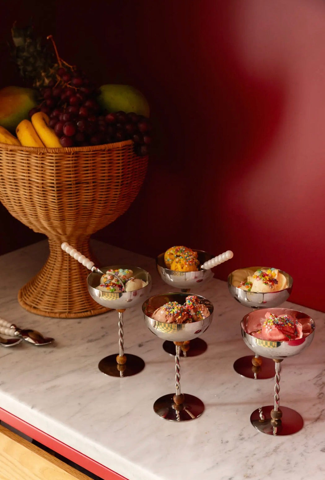 Beth Decoration Bowl with fruit in background, silver ice cream coupes with sprinkles in foreground on marble surface
