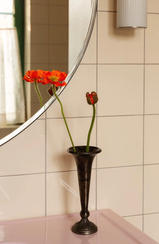 Othea Trumpet Vase styled with red poppies and tulips on pink bathroom shelf in front of round mirror and white tiles