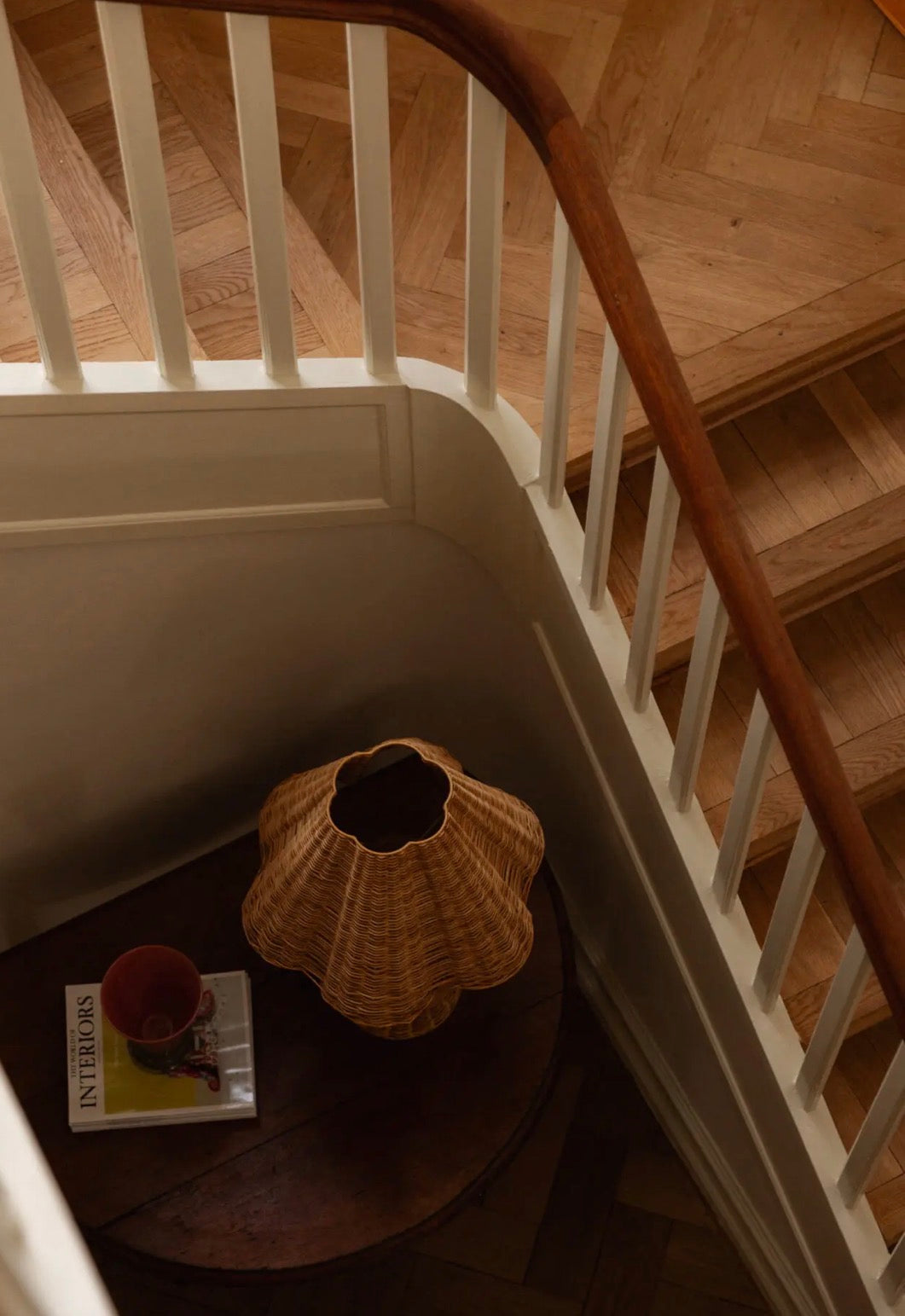 Bani Table Lamp shade styled as decorative object on dark wood side table beneath staircase with Interiors book