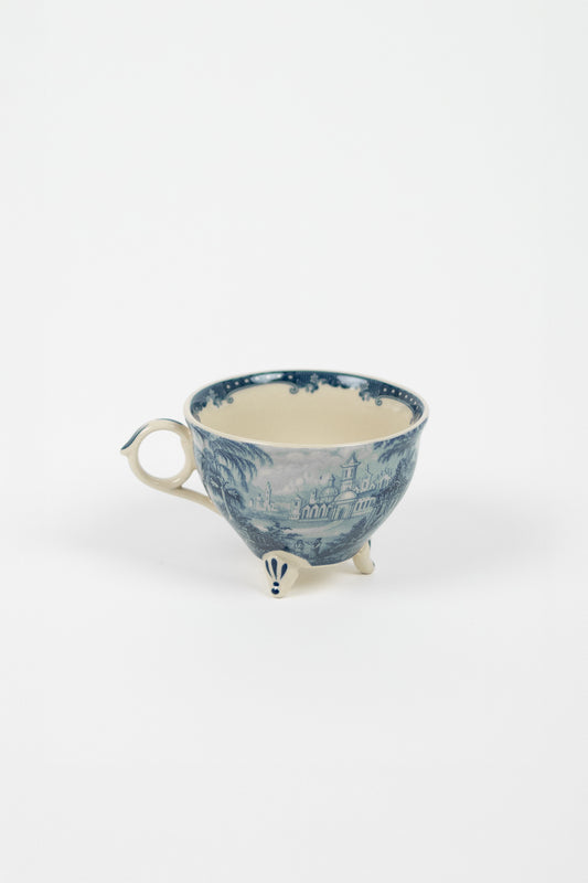 Estelle Cup Blue — wide stoneware cup with blue toile de Jouy pattern on three feet, round loop handle, on white background